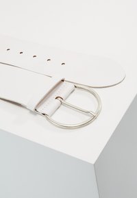 White leather belt with a silver circular buckle and multiple holes for adjustment. Flat, smooth texture with a clean design.