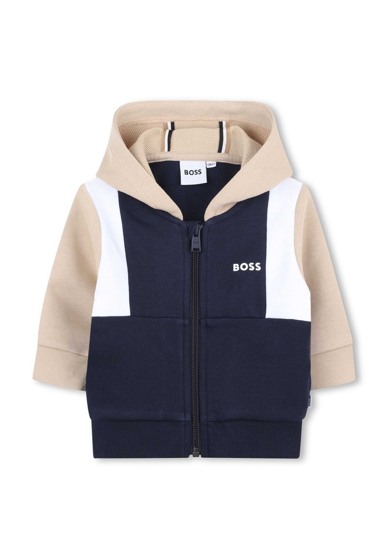 Hoodie zippé bleu marine et beige avec une bande blanche contrastante, des poignets côtelés et une capuche. Présente le logo "BOSS" sur la poitrine. Texture de tissu douce.