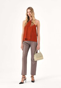 Bezrękawnik w kolorze rdzy z asymetrycznym dołem, zestawiony z dopasowanymi szarymi spodniami z eko skóry. Do tego beżowa torebka z wzorzystymi akcentami.
