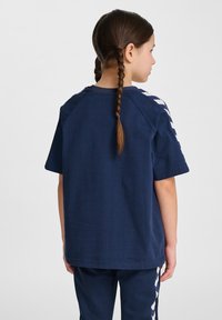 T-shirt di cotone blu navy con maniche corte e dettagli bianchi a zigzag lungo le spalle. Texture liscia, vestibilità comoda, collo a giro.