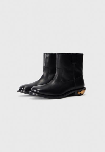 Svarta läderankelboots med en mjuk textur, rund tå och en distinkt guldfinish på klacken. Har en låg staplad klack.