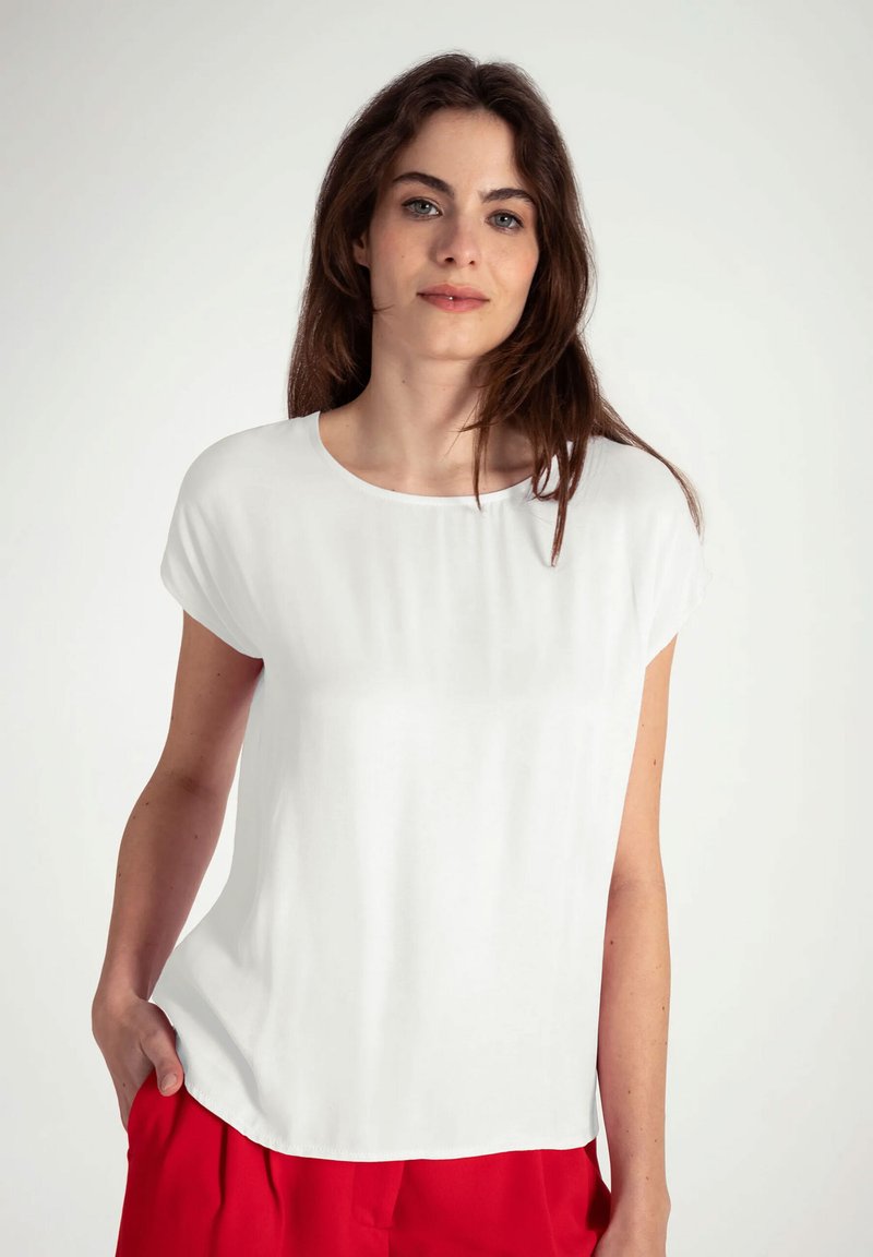 Witte T-shirt met korte mouwen en een ronde hals, gladde textuur en een ontspannen pasvorm, gecombineerd met rode broek voor contrast.