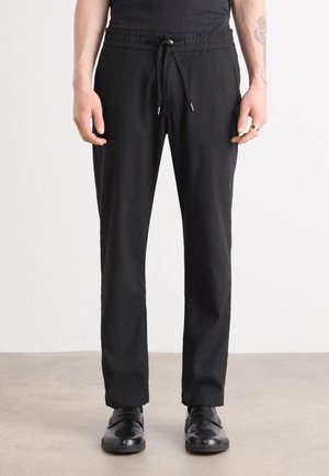 Black linen pants with an elastic waistband, adjustable drawstring, tapered legs, and side pockets, worn with black shoes.
