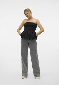 Svart strapless peplumtop med texturerad tyg och framfickor, kombinerad med högmidjade grå jeans och spetsiga beige skor.