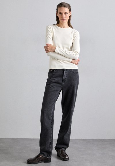 Light cream long-sleeve shirt, paired with high-waisted dark gray jeans. The outfit is completed with dark brown loafers. Simple and minimal design.