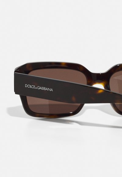 Ochelari de soare din tortoiseshell cu rame unghiulare și lentile maro. Prezintă un braț negru îndrăzneț, cu branding alb "DOLCE & GABBANA".