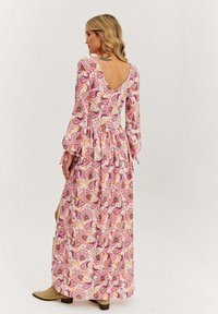 Maxi šaty v růžové barvě s květinovým vzorem, dlouhými rukávy, V-zadním výstřihem, rozšířenou sukní a manžetami. Materiál vypadá lehce a má volný střih.