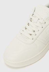 Adidași din piele albă cu finisaj texturat, vârf rotund, design cu șireturi și branding embosat pe limbă și lateral.