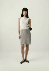 Top branco sem mangas com textura canelada, combinado com uma saia cinza ajustada, apresentando uma textura suave. Uma bolsa preta e sapatos planos completam o look.