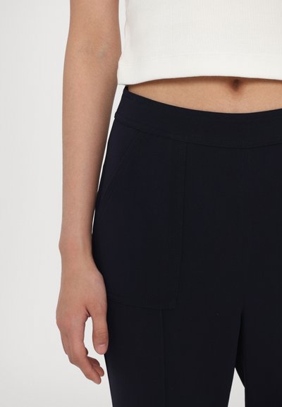 Marineblå bukser med en glat tekstur, udstyret med frontlommer og en bred talje. Sammen med en hvid cropped top.