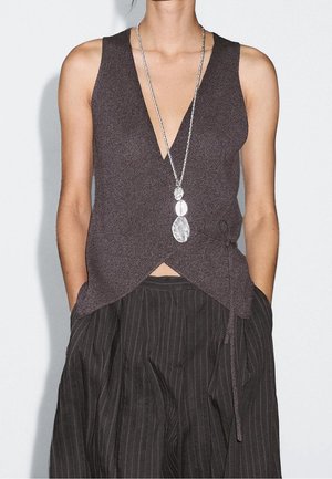 Haut en maille foncé sans manches avec un profond col en V, ourlet asymétrique, associé à un pantalon ample à fines rayures foncé et un long collier pendentif argenté.