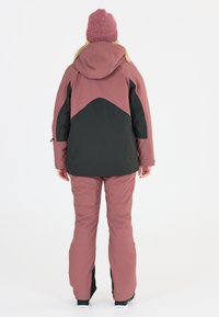 Lumihousut ja takki pinkki-mustassa suunnittelussa. Varustettu hupulla ja elastisilla hihoilla, joissa on sileä rakenne ja kestävä kangas.