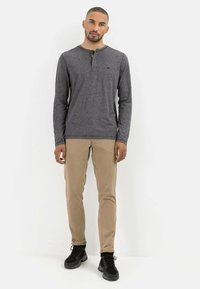 Grå langærmet henley skorte med knapper, parret med khaki slim-fit bukser og sorte sko, stående foran en hvid baggrund.
