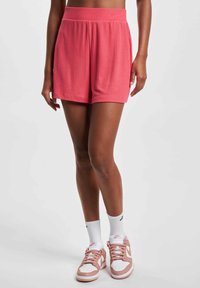 Rosa gerippte Shorts mit elastischem Bund, kombiniert mit weißen und hellrosa Sneakers sowie weißen Socken. Glatte Textur, lässige Passform.