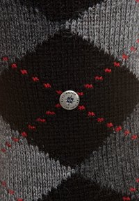 Stricksocken mit einem diagonalen Rautenmuster in Schwarz, Grau und Rot, akzentuiert mit einem runden Burlington-Logo. Weiche Textur und Wärme.