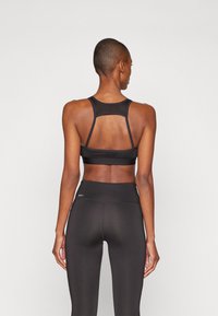 Svart sport BH med brede stropper og racerback-design, kombinert med høydejusterbare sorte tights. Glatt stoff med en jevn tekstur.