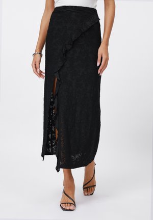 Jupe maxi en dentelle noire avec un côté volé, présentant une fente haute. Fabriquée dans un tissu texturé, conçue pour une silhouette fluide.
