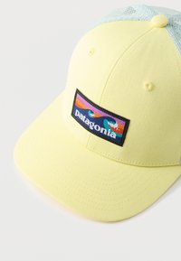 Κίτρινο και ανοιχτό μπλε πλεκτό καπέλο μπέιζμπολ με ένα πολύχρωμο σήμα λογότυπ ο της Patagonia στην εμπρόσθια πλευρά.