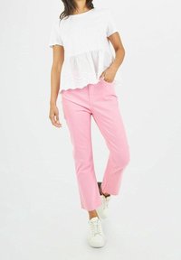 Haut peplum blanc avec bordure en œillets et manches courtes, associé à un pantalon droit rose clair. Modèle portant des baskets blanches.