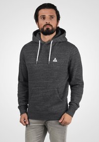 Sudadera gris de tela suave, con un bolsillo canguro en la parte delantera, cordones blancos y un pequeño logo triangular en el pecho.