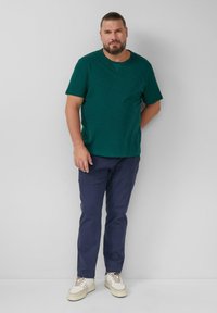 Donkergroene crewneck t-shirt, lichtgewicht, gecombineerd met marineblauwe broek en gebroken witte sneakers. Eenvoudig ontwerp zonder duidelijke patronen of accenten.