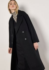 Schwarzer Doppelreiher-Mantel aus einer Wollmischung, mit großen Reverskragen, Knopfdetails und leicht oversized Passform.