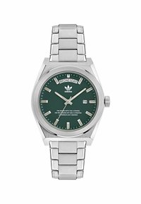 Montre en acier inoxydable avec un cadran vert, des index argentés, un affichage jour/date et un bracelet en maillons argentés. Présente le logo Adidas en haut.