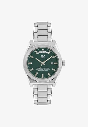 Zegarek ze stali nierdzewnej z zieloną tarczą, srebrnymi znacznikami godzin, wyświetlaczem dnia/datą i bransoletą z srebrnych ogniw. Posiada logo Adidasa na górze.