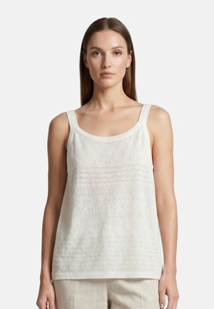 Femme portant un top en maille blanc sans manches avec un col rond et un motif texturé subtil, associé à un pantalon clair.
