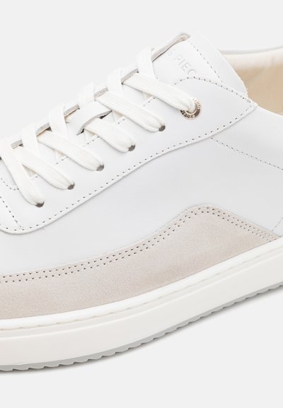 Baskets blanches en cuir avec des accents en suède beige, lacets plats blancs, détails brodés et une semelle en caoutchouc texturée. Design minimaliste.