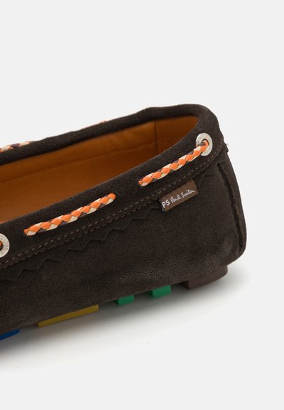 Chaussure slip-on en daim marron avec des lacets tressés orange, intérieur beige et accents colorés de semelle en caoutchouc bleu, vert, jaune et marron.