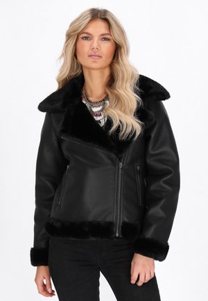 Veste en simili cuir noir avec un col et des poignets en fourrure, dotée d'une fermeture éclair et de poches latérales. Texture lisse et design ajusté.