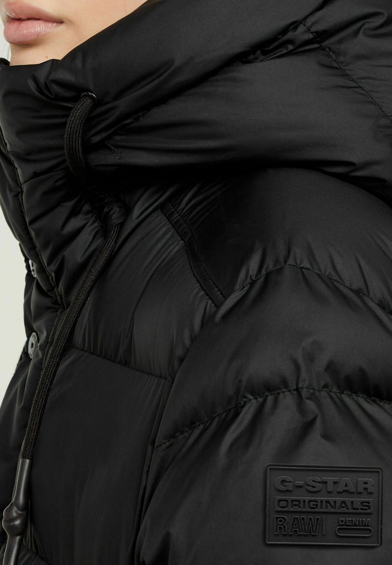 Nahaufnahme einer Person, die eine schwarze G-Star Originals gepolsterte Jacke mit hohem Kragen und verstellbaren Kordeln trägt.