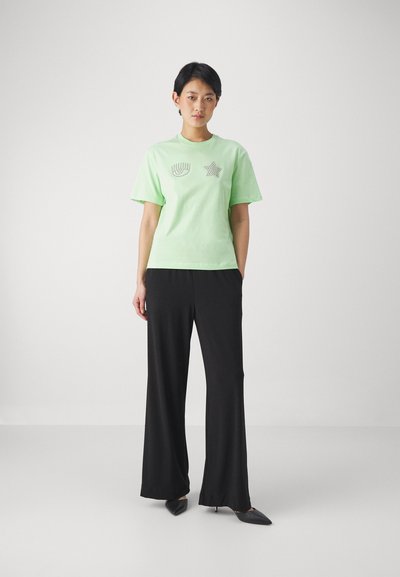 Mint green short-sleeve t-shirt with graphic designs in silver. Paired with black wide-leg pants and pointed black heels. Smooth textures.