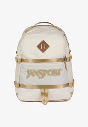 Beżowy plecak JanSport z dwoma poziomymi paskami, górnym uchwytem do przenoszenia, przednią kieszenią na zamek i brązową łatką w kształcie diamentu.