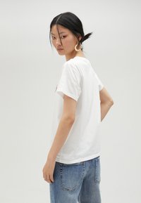 Camiseta de algodón blanca, con mangas cortas, escote redondo y estampado gráfico rojo en el frente; combinada con jeans de color azul claro.