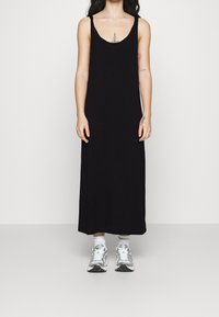 Svart ärmlös maxiklänning i mjukt tyg, med rundad halsringning. Matchas med silverfärgade sneakers och vita strumpor.