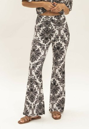 Pantalons évasés noir et blanc à motif en tissu léger, arborant un design damassé. Associés à des sandales à lanières marron.