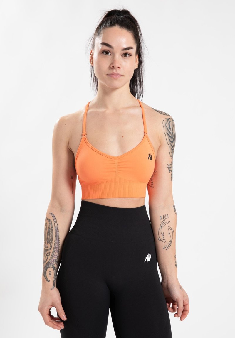Oranje sportbeha met dunne bandjes, gerimpelde voorkant en een aansluitende band. Gecombineerd met hooggerande zwarte leggings met een klein logo.