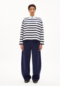 Sudadera de rayas en azul marino y blanco con mangas anchas, combinada con pantalones sueltos en azul marino. Tejido texturizado y pequeño detalle del logo en blanco en el pecho.