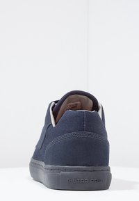 Marinblå sneaker med grå sula, synliga sömmar, vadderad krage och "G-STAR RAW" präglat på hälen.