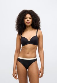 Μαύρο επενδεδυμένο σουτιέν με ρυθμιζόμενους ιμάντες, με απαλό υφή. Μαύρο σλιπ με αντίθετη εκρού ζώνη μέσης.