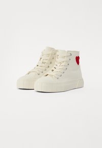 Höga sneakers, krämfärgad kanvas, snörningsdesign, gummisula och texturerad mellansula; har en broderad röd hjärta på sidan.