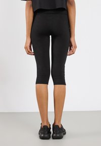 Czarne legginsy capri wykonane z elastycznego materiału o gładkiej strukturze, z dopasowanym fasonem, sięgającym do połowy łydki.