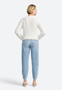 Pull en laine blanc avec un motif texturé, coupe courte, et manches longues associé à un jean taille haute bleu clair et des chaussures beiges.