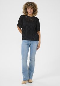 Black lace top with short, puffed sleeves, scalloped edges, and a floral pattern, paired with light blue flared jeans and beige shoes.