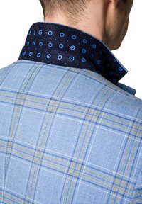 Jasnoniebieska koszula w kratę z kontrastowym ciemnoniebieskim kołnierzykiem w wzór kropkowany. Widoczne szwy i faktura materiału.