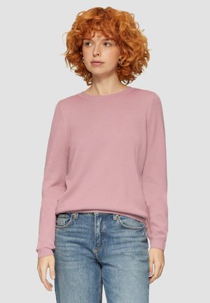 Pull rose clair avec un motif de tricot texturé, col rond et manches longues. Associé à un jean bleu, mettant en valeur une coupe décontractée.