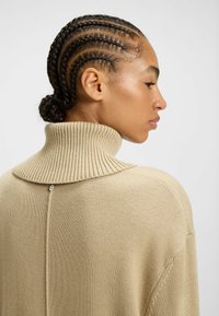 Beiger Strickpulli mit hohem Rippkragen, der mit einem Knopfakzent am Rücken und einer lässigen Passform ausgestattet ist. Texturiertes Material, weicher Stoff.