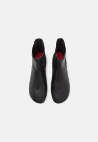 Botas de tobillo de cuero negro con textura suave, punta redondeada y laterales con cortes. Las plantillas rojas son visibles desde la vista superior.